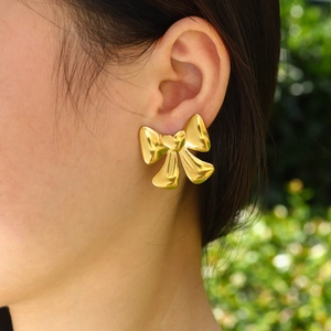 Eleganti orecchini a fiocco placcati in oro 18K indossati da una modella su sfondo verde