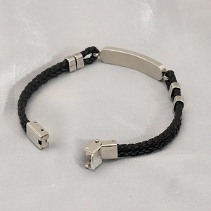 Détail macro du bracelet tressé en cuir noir avec plaque d'identité incurvée en acier inox