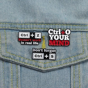 Detail of creative Ctrl+Z, Ctrl+O, Ctrl+S enamel pins on a blue denim jacket pocket