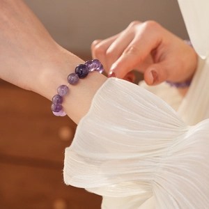 Detail eines lila Amethyst-Perlenarmbands am Handgelenk mit warmem Licht und weißem Stoff