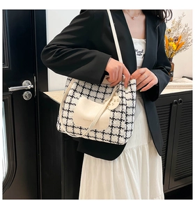 Close-up of black and white houndstooth tote bag featuring a cat charm and fashion logo