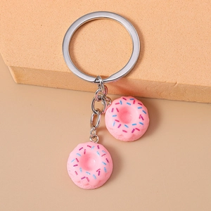 Detailed view of pink resin donut charms with metal keyrings on a beige sponge surface