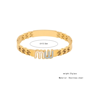 Macro view of gold stainless steel bangle with leaf patterns and enamel MW lettering details