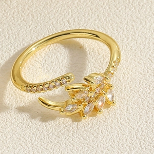 Dettaglio dell'anello regolabile placcato oro con spiga di grano e zirconi su tessuto beige