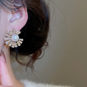 Close-up of a pearl earring with radiating zircon stones worn on an earlobe