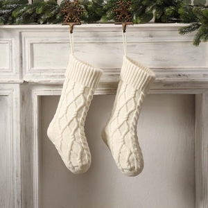 Pair of cream white cable knit Christmas stockings hanging on a festive mantelpiece