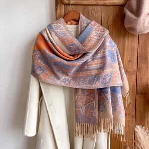 Detail of bohemian paisley jacquard scarf with orange and blue fringe on a white coat