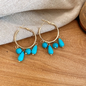 Detail of gold hoop earrings with turquoise beads and teardrop tassels on wood texture