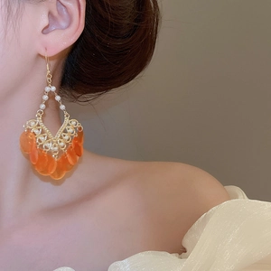 Detail view of pearl tassel earrings with orange translucent drops on model ear