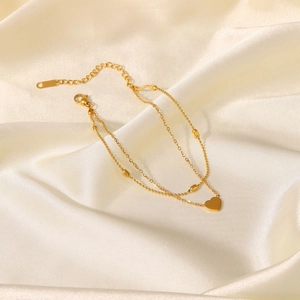 Double-layered 18K gold heart pendant anklet with oval bead chain on soft silk background