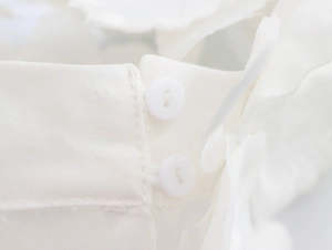 Macro detail of elegant white organza shirt showing fine stitching and white round buttons