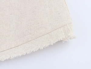 Macro shot of beige faux linen fabric with raw fringe edges and neat stitching details