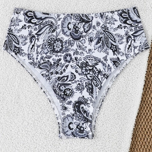 Detail of high waisted bikini bottoms with intricate black paisley print on white fabric