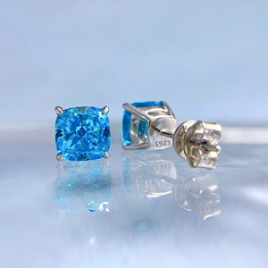 Macro shot of 925 silver stud earrings featuring cushion-cut blue gemstones in 4-prong setting