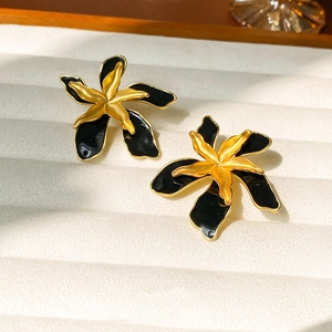 Detailed view of vintage gold and black floral enamel earrings on a textured jewelry tray