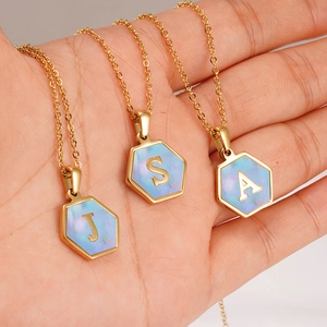 Close-up of hexagonal 18K gold-plated initial pendants with iridescent mother of pearl