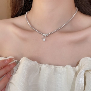 Détail d'un collier en perles grises avec pendentif étoile et zircone porté par un modèle