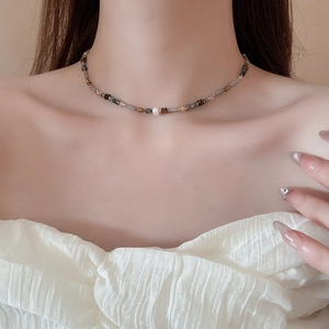 Close-up of beaded necklace with ceramic beads and pearl pendant on model neck