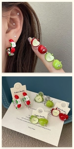Detail of asymmetrical apple earrings with red and green enamel and crystal accents
