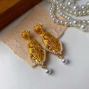 Detail of vintage gold hollowed-out earrings with intricate floral patterns and dangling pearls