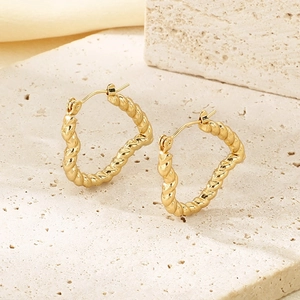 Macro detail of gold twisted rope hoop earrings with buckle closure on beige stone texture