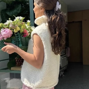 Detailed knit texture of a white sleeveless turtleneck vest in a bright indoor setting