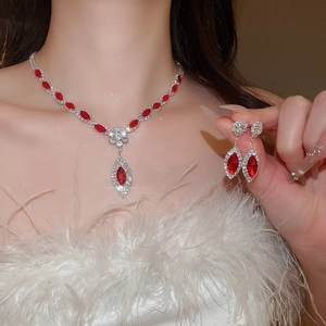 Close-up of floral silver necklace and drop earrings with red gems and sparkling rhinestones