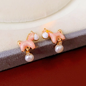 Detailed view of horse stud earrings with pink enamel and hanging pearl on jewelry tray