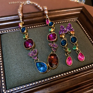 Vintage jewelry set with colorful gemstones and pearls displayed in an ornate wooden frame