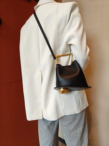Detail of black leather bucket bag with gold handle and adjustable shoulder strap