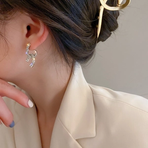Detail of silver knot earrings with sparkling cubic zirconia on model wearing a beige blazer