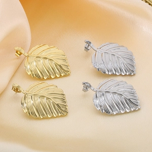 Macro shot of gold and silver leaf earrings with realistic textures on elegant champagne silk