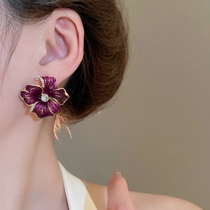 Gros plan d'une boucle d'oreille fleurie violette avec bords dorés et zircon sur mannequin
