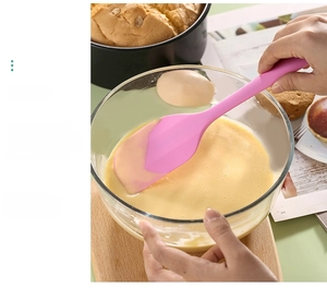 Pink silicone spatula mixing cake batter in a glass bowl for professional baking tasks