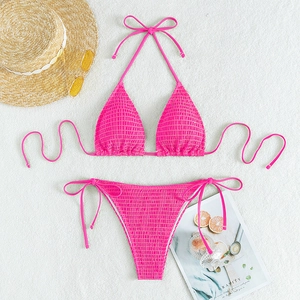 Flat lay of rose red smocked bikini set with straw hat and sunglasses on white sand