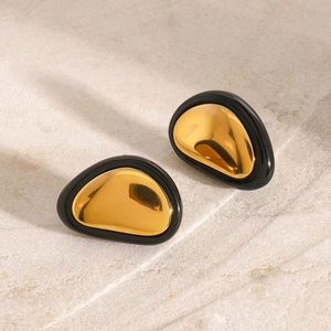 Detail view of vintage style gold pebble earrings with black borders on stone surface