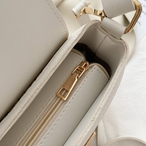 Close-up of golden zipper closure and adjustable strap hardware on cream shoulder bag