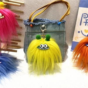 Macro shot of fluffy yellow monster keychain with green pom-poms on blue denim bag