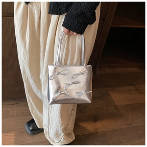 Detail of silver square handbag featuring metallic faux leather and silver bow accents