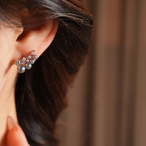Detail of 18k gold plated earrings featuring grey pearls and sparkling zircon accents