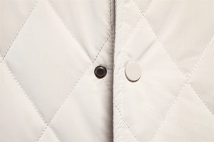 Macro detail of diamond quilted jacket featuring round metal snap button and ripstop fabric