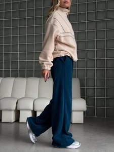 Détail d'un sweat en polaire beige demi-zip et d'un pantalon large bleu sarcelle
