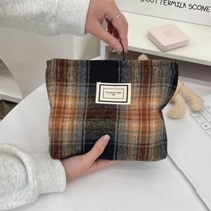 Detail of yellow and black plaid wool makeup bag with metal zipper and cloth label