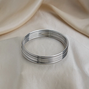 Macro shot of polished silver stainless steel bangles layered on soft champagne silk fabric