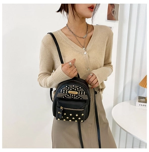 Detail view of a black punk style mini backpack with gold studs and zipper on a model