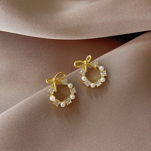 Elegant gold bow earrings with pearls and crystals on dark silk background