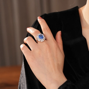 Dettaglio anello vintage con gemma blu ovale e alone di diamanti indossato al dito