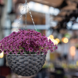 Artificial purple flowers in a dark grey woven hanging basket with metal chains
