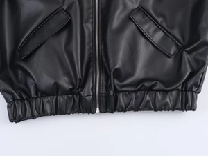 Detail of black faux leather jacket showing metal zipper, pocket and stitched hem