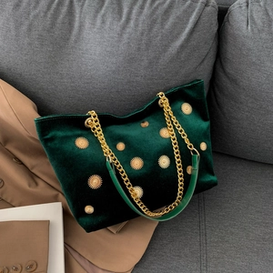 Dark green velvet tote bag with gold floral rivets and chain strap on a grey sofa